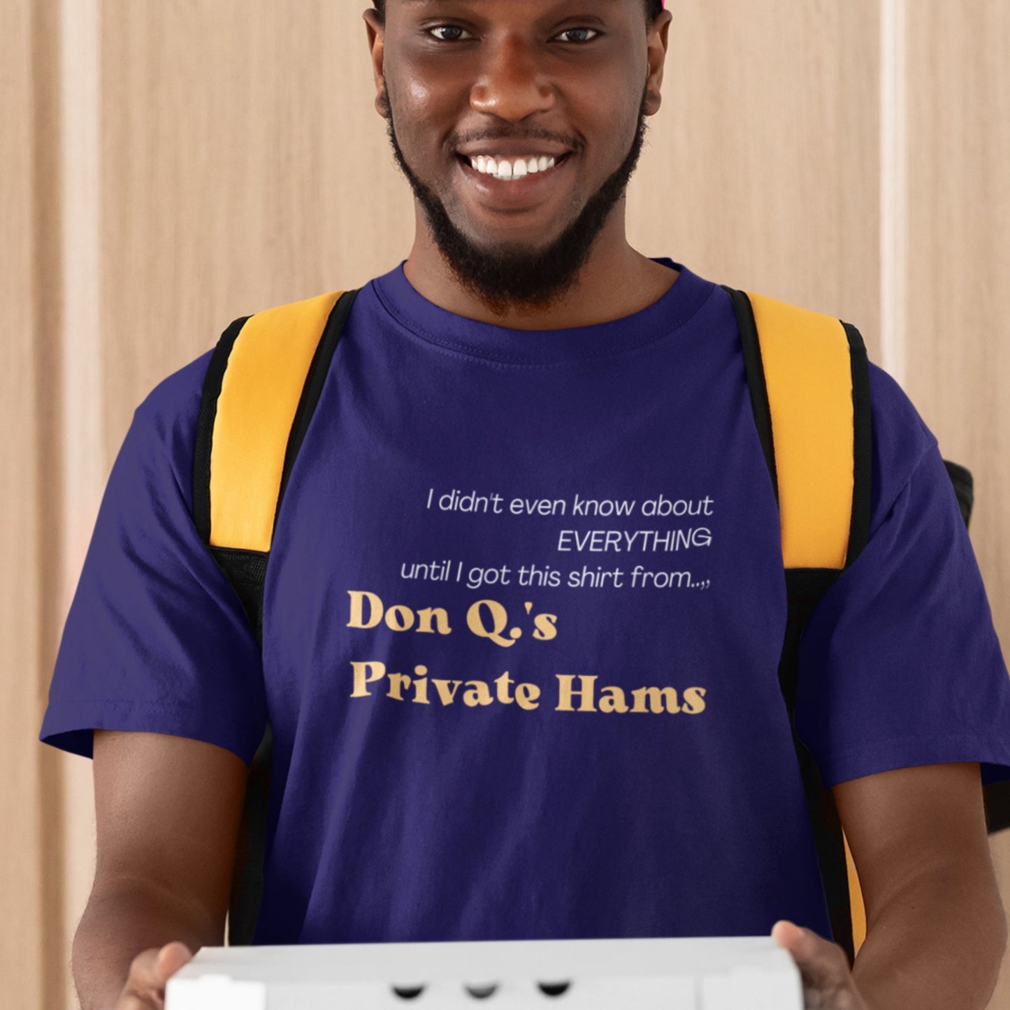 Man wearing a navy blue t-shirt with humorous text, holding a white box.
