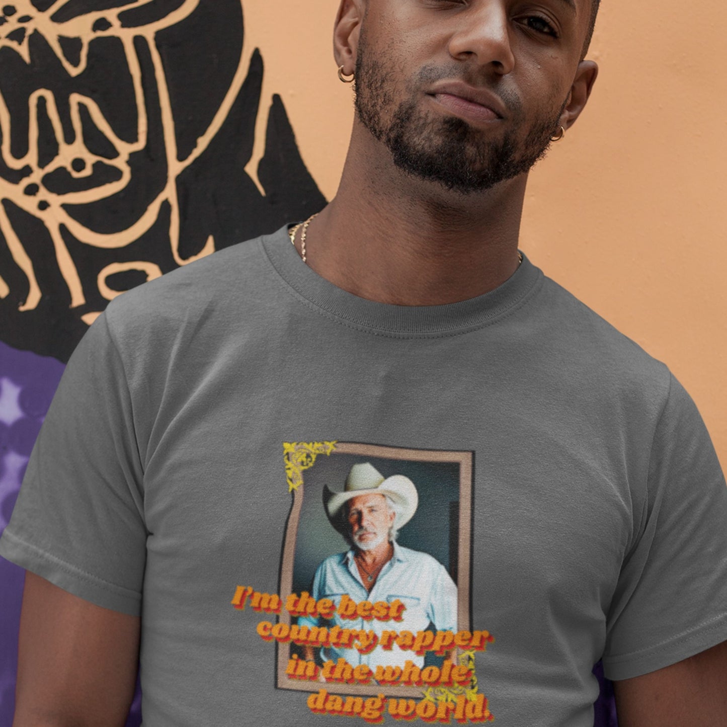 Man wearing a t-shirt with a graphic of a man in a cowboy hat and text, against a colorful background.
