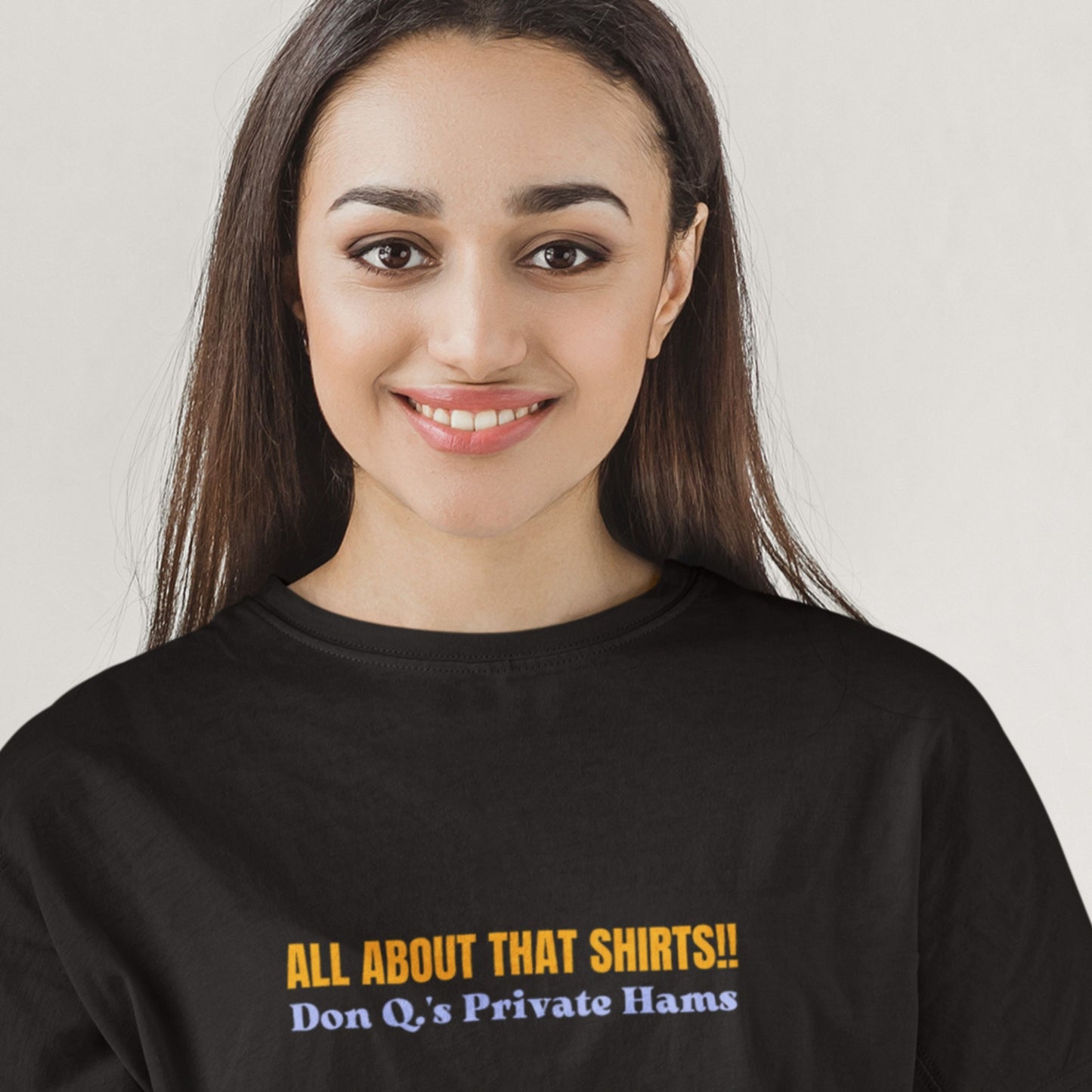 Smiling woman wearing a black t-shirt with multicolored 'all about that shirts!!' text on a beige background.
