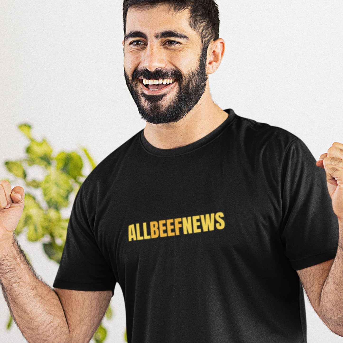 Celebrating man wearing a black t-shirt with humorous colorful ALLBEEFNEWS text in a living room.