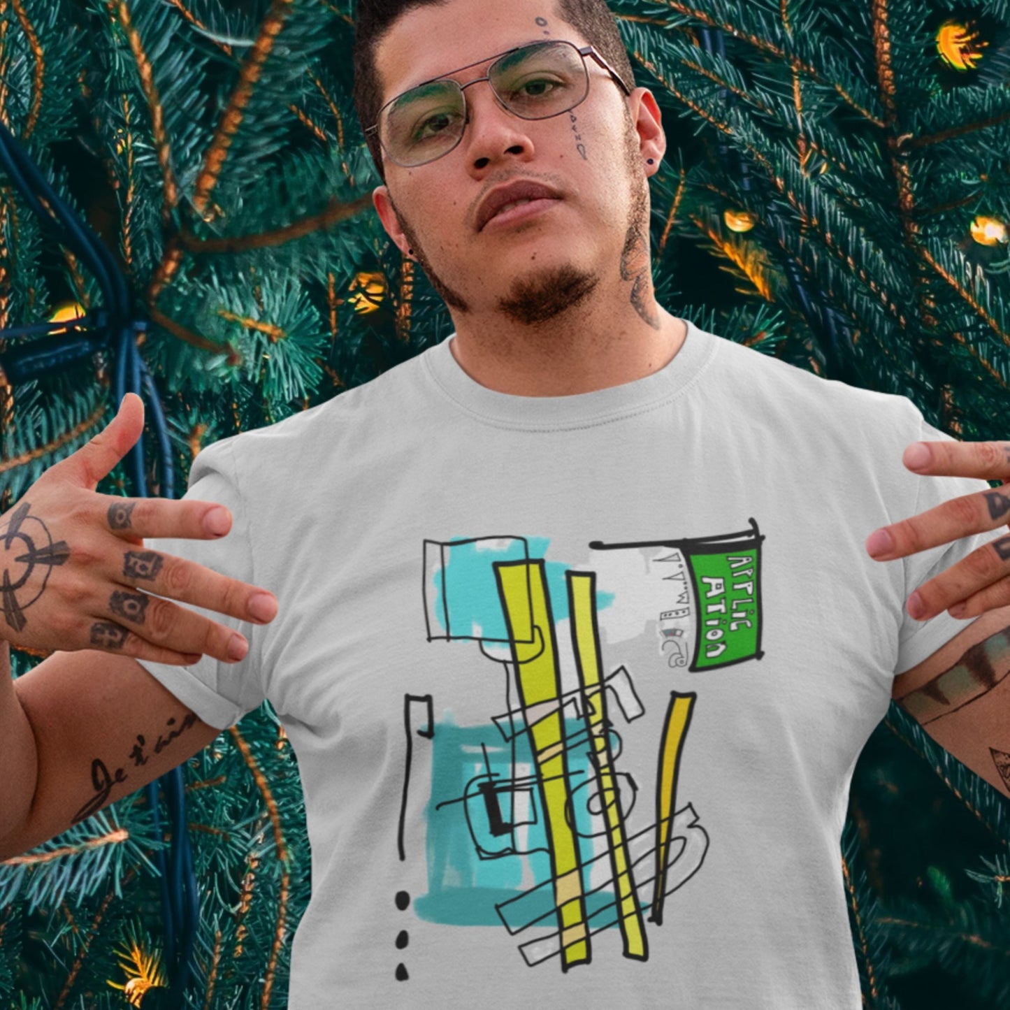 Tough guy wearing a light grey t-shirt with a colorful abstract drawing in front of a giant tree.