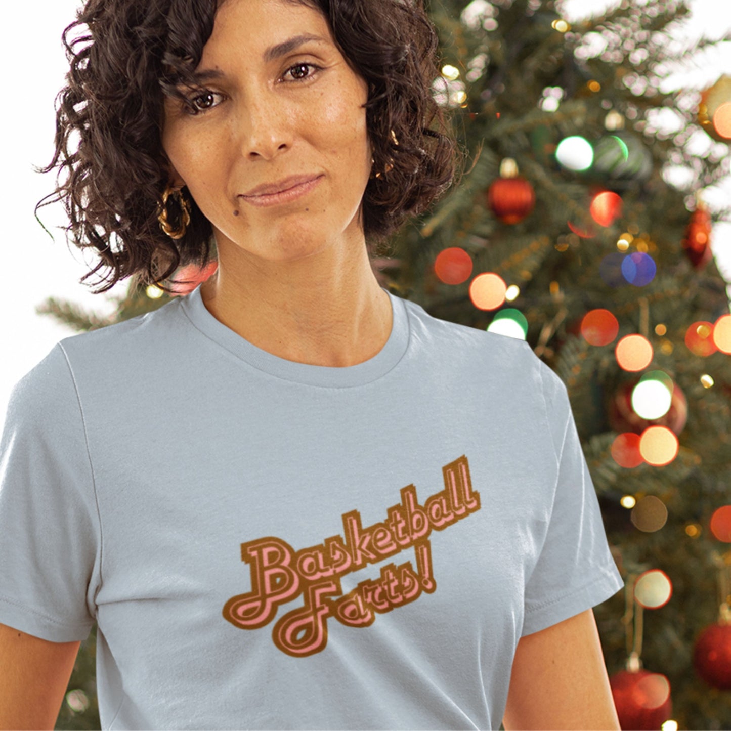 Christmas woman wearing a light blue t-shirt with two-tone red text reading 'Basketball Farts!' in front of a Christmas tree.