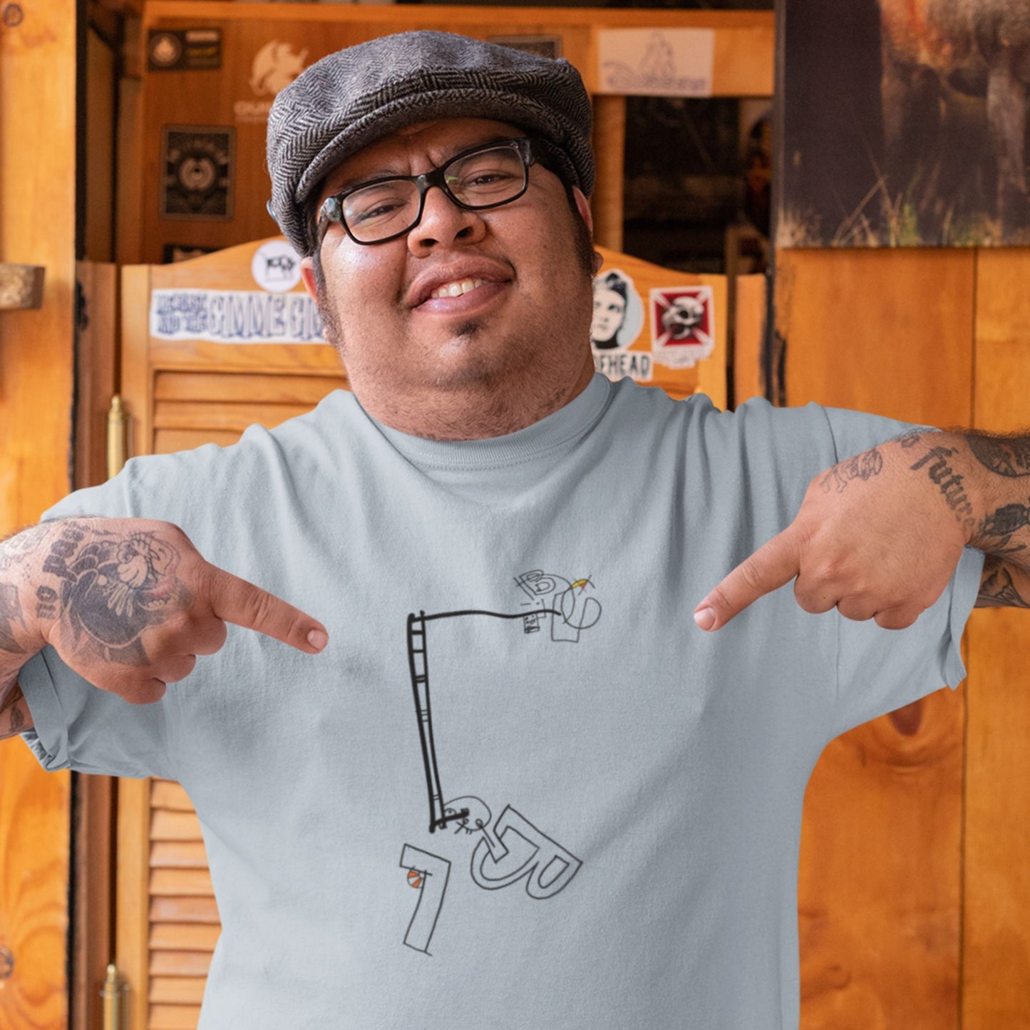 Man pointing to a graphic on his light blue t-shirt with a wooden background
