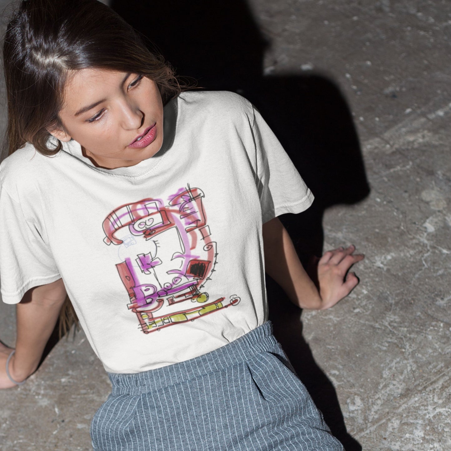 Person wearing a white t-shirt with a colorful graphic design sitting on the ground.