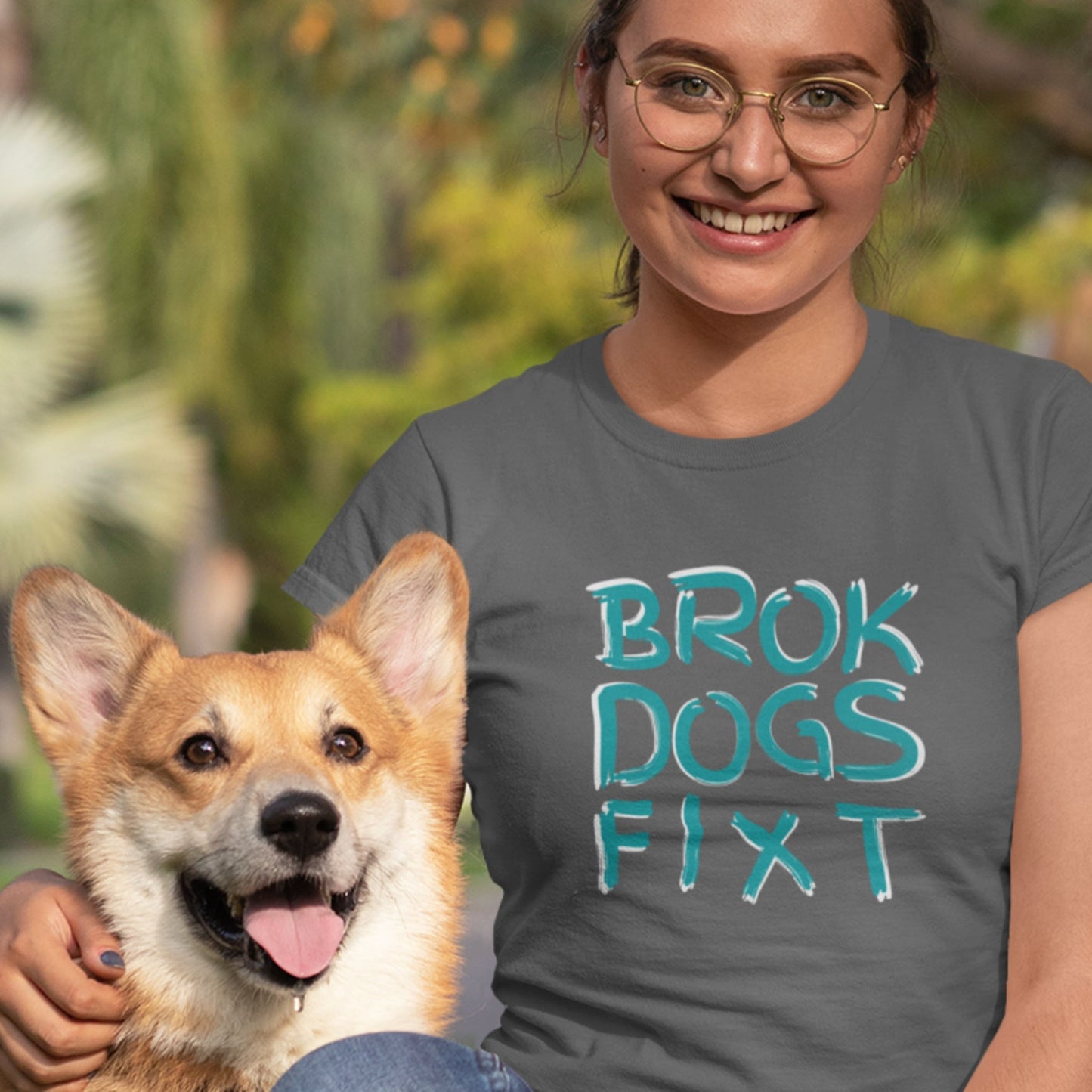 Person wearing a t-shirt with 'BROK DOGS FIXT' text, holding a dog outdoors.