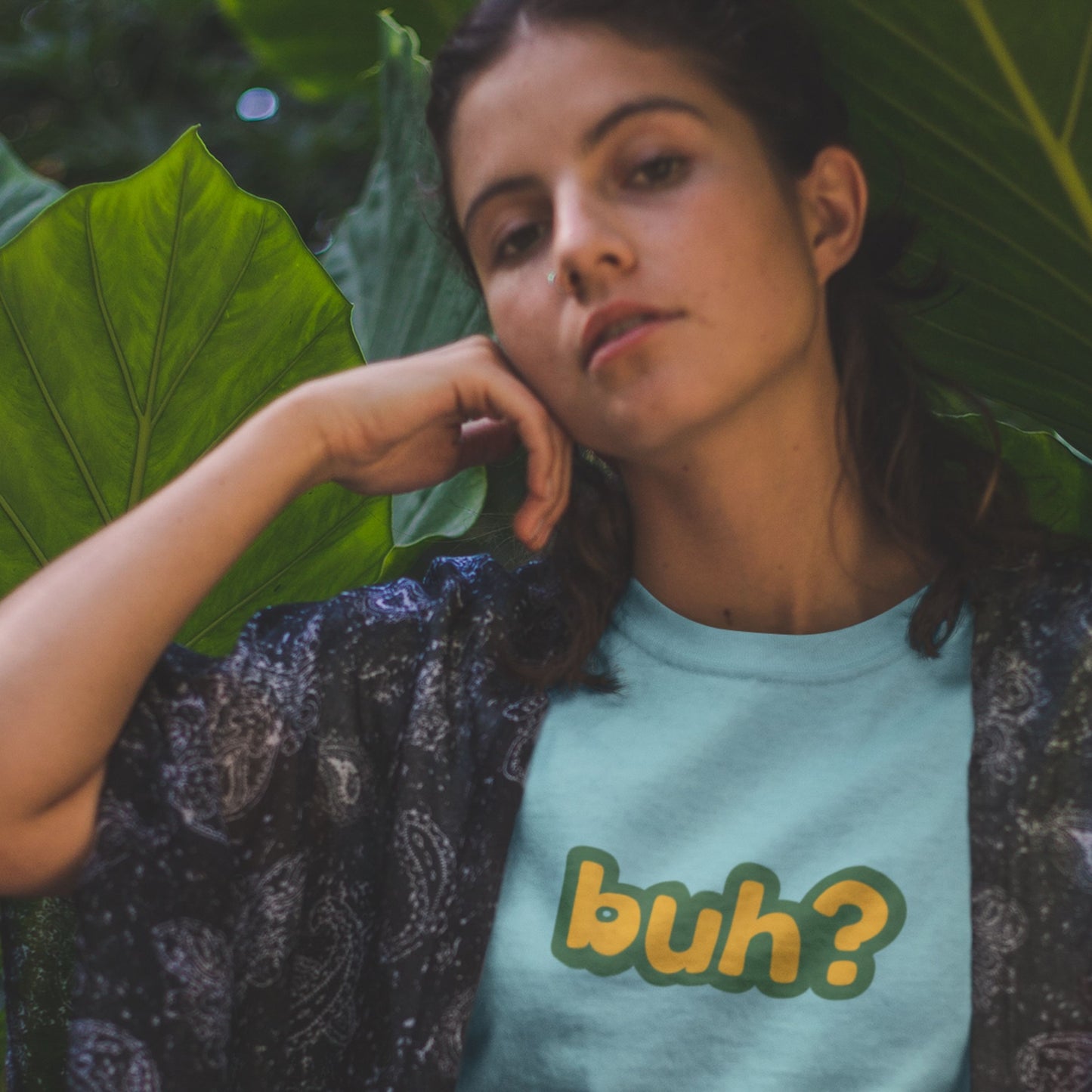 This lady in the plants wearing a turquoise blue t-shirt with multicolored 'buh?' text.
