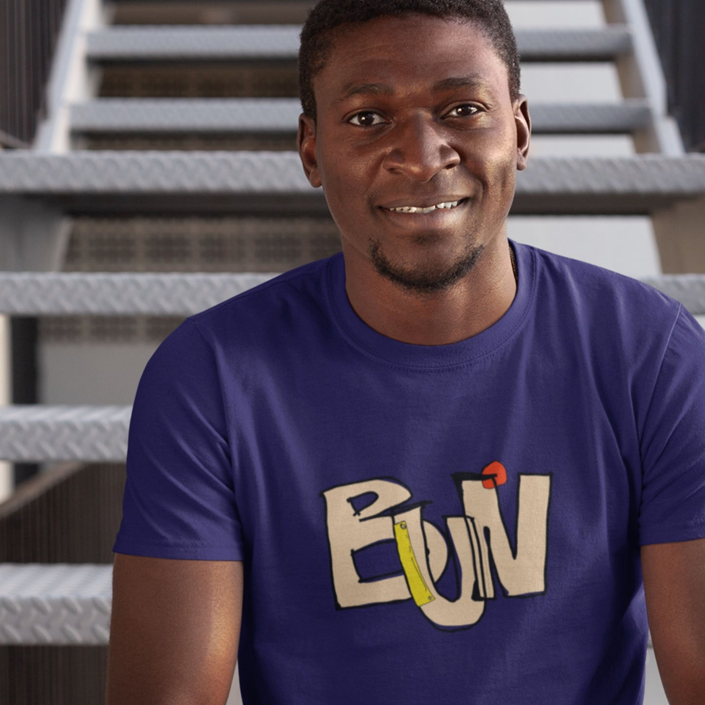 Man wearing a purple t-shirt with a colorful logo sitting on steps.