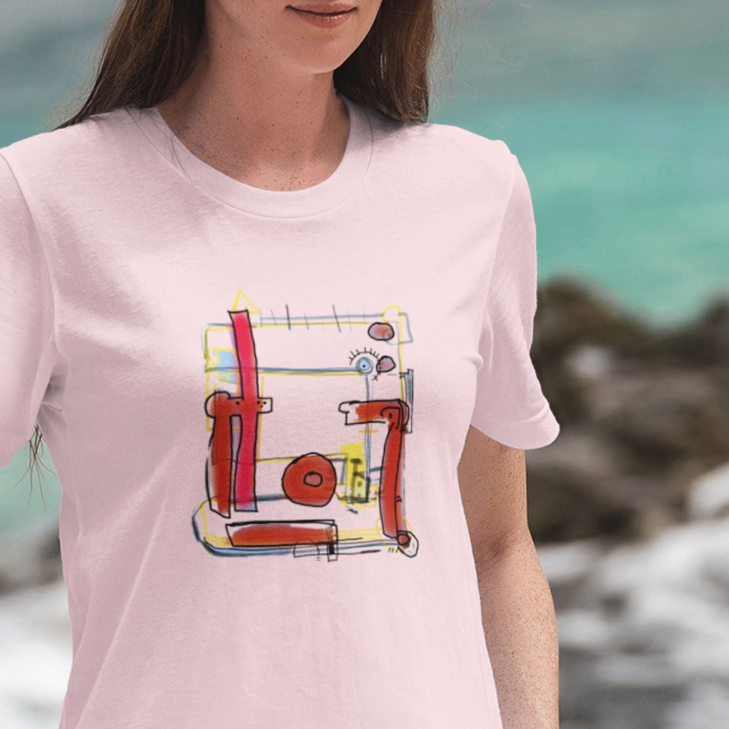Woman wearing a pink t-shirt with a colorful abstract drawing on a beach.