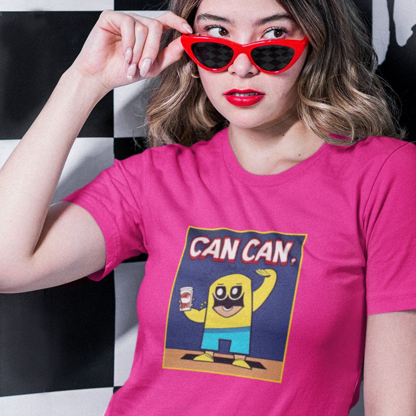 Woman wearing a pink t-shirt with a graphic design and red sunglasses, standing against a black and white checkered background.