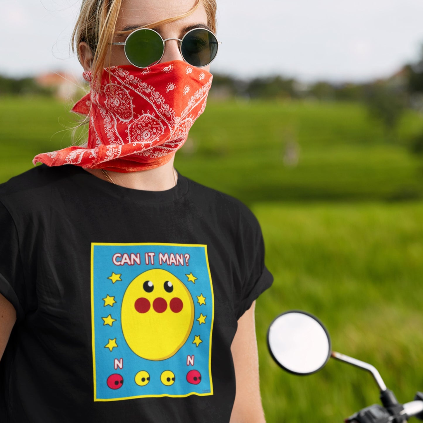 Person wearing a black t-shirt with a colorful graphic and red bandana outdoors.