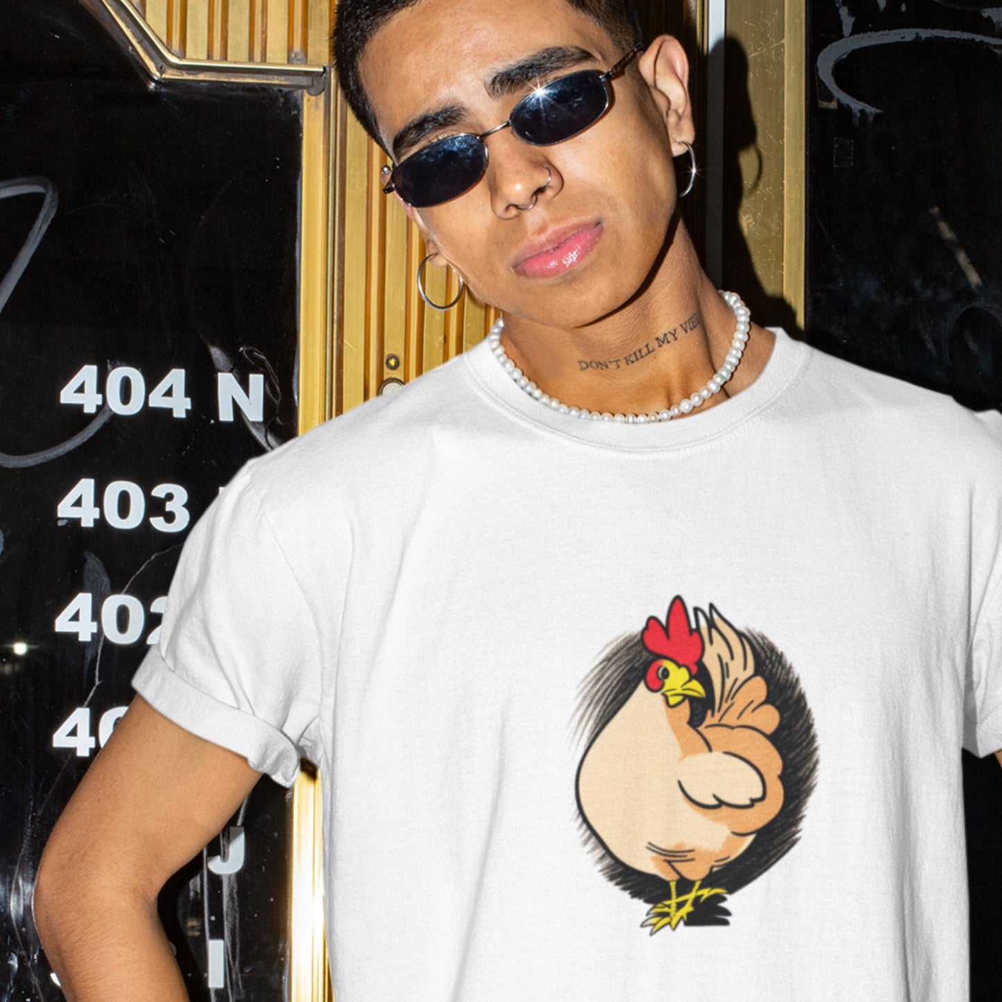 Man wearing a white shirt with a colorful rooster illustration in a bar.