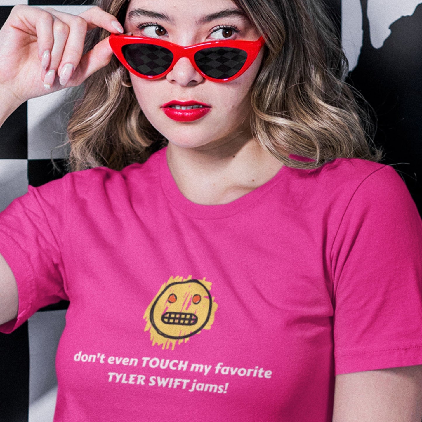 Person wearing a pink t-shirt with a sun graphic and text, holding red sunglasses.