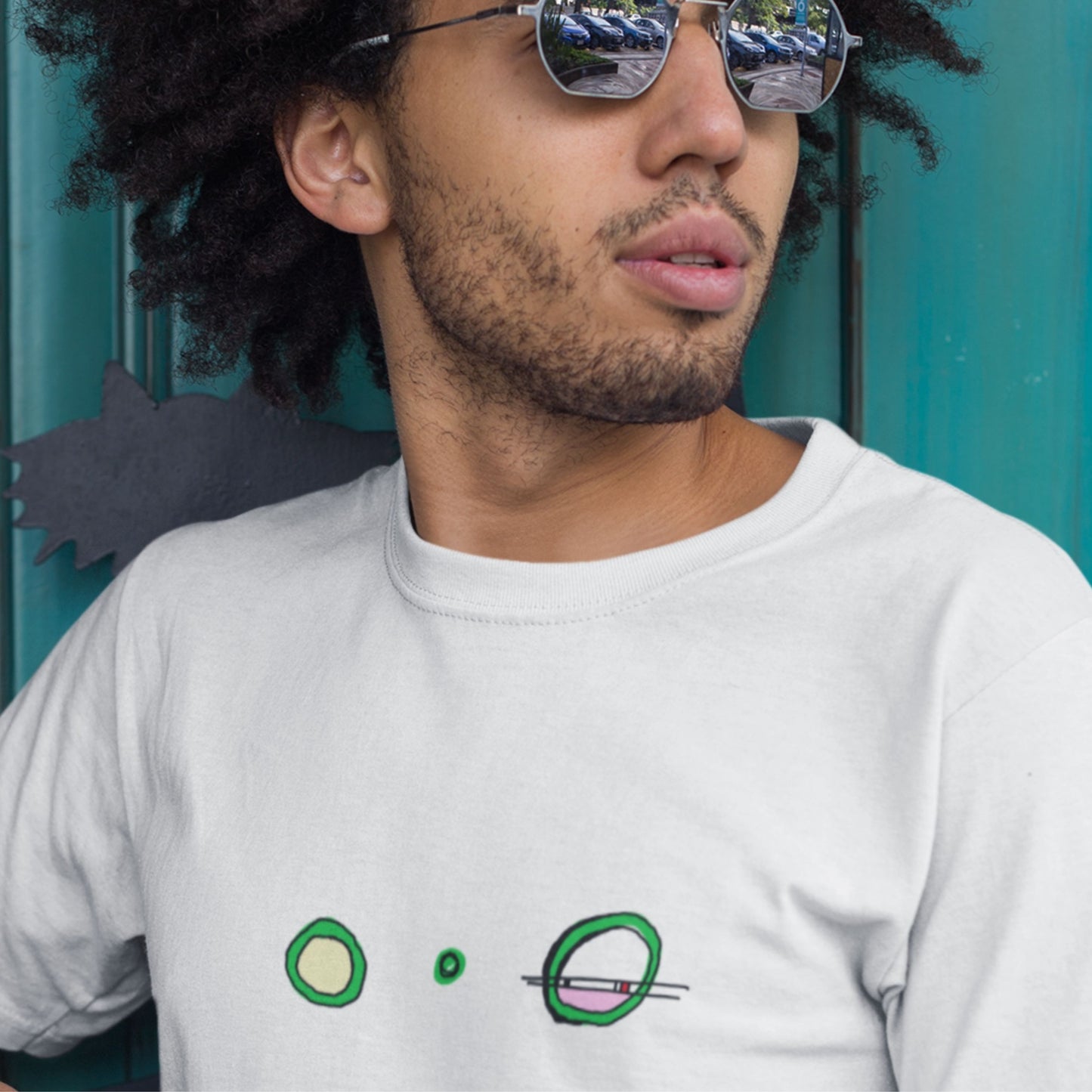 Person wearing a white t-shirt with green designs in front of a teal background