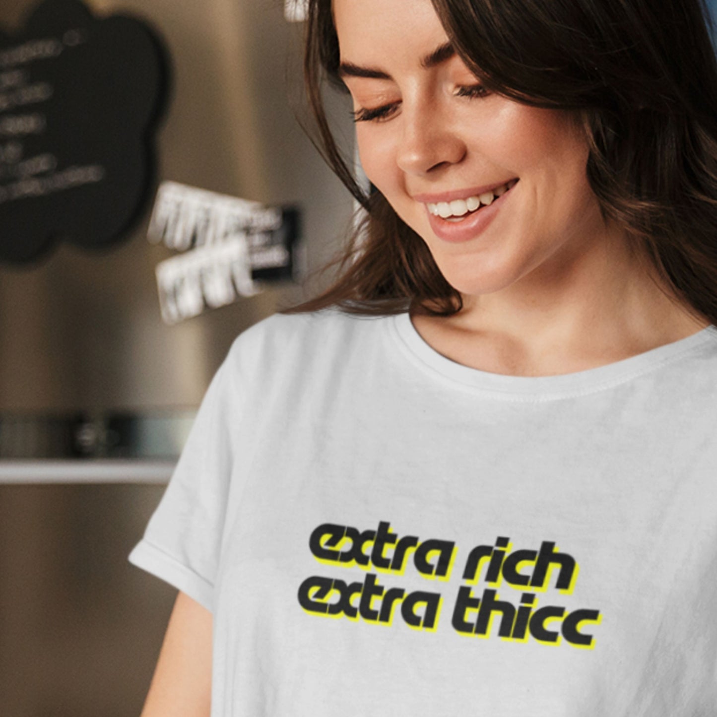 Woman wearing a light grey t-shirt with 'extra rich extra thicc' text in a casual setting.