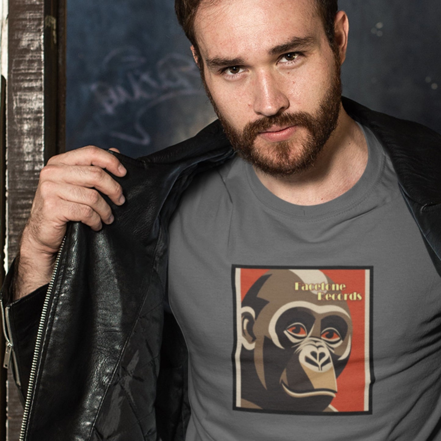Man wearing a gray t-shirt with a graphic design of a monkey and text, holding a black leather jacket.