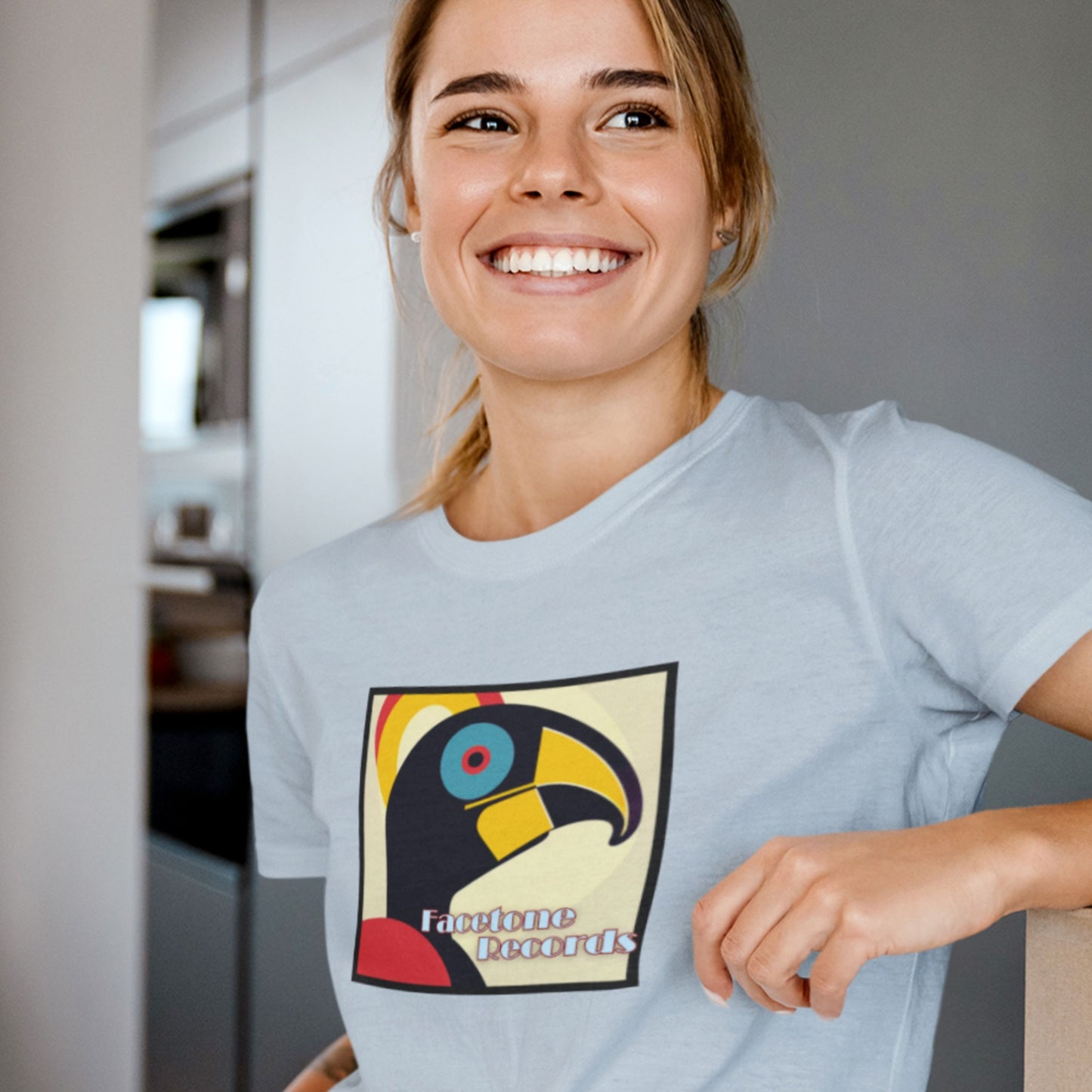 Woman wearing a light blue t-shirt with a colorful graphic hornbill design in a kitchen setting