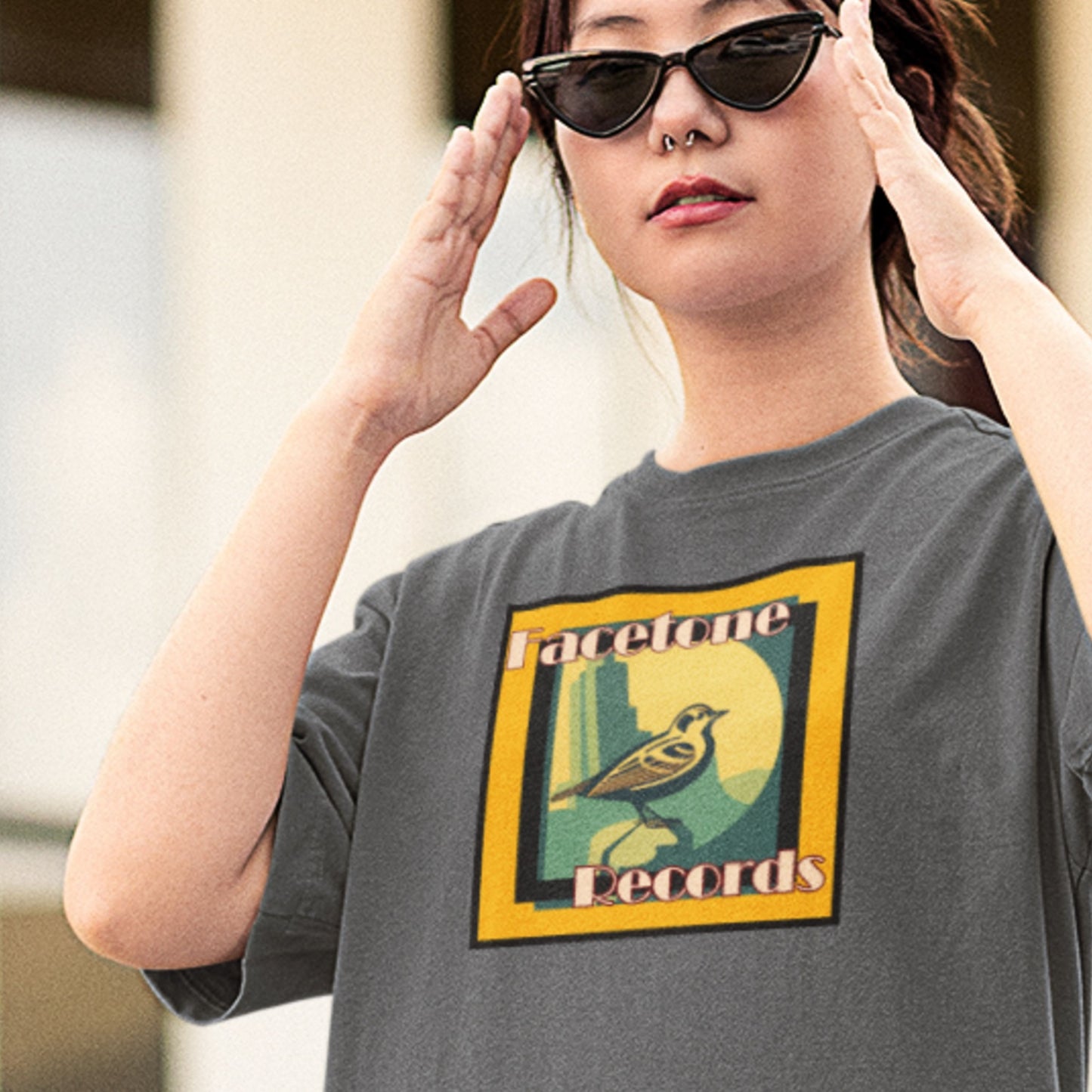 Person wearing a gray t-shirt with a graphic design and sunglasses, standing outdoors.