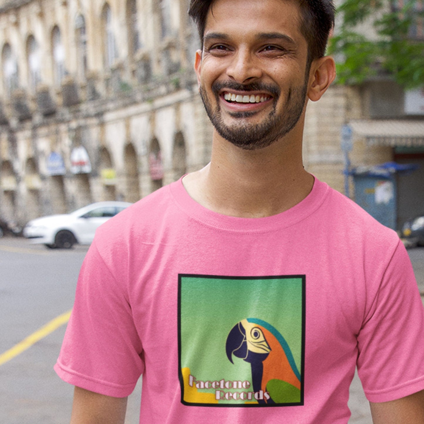 Man wearing a pink t-shirt with a parrot graphic and 'Facetone Records' text on a city street.