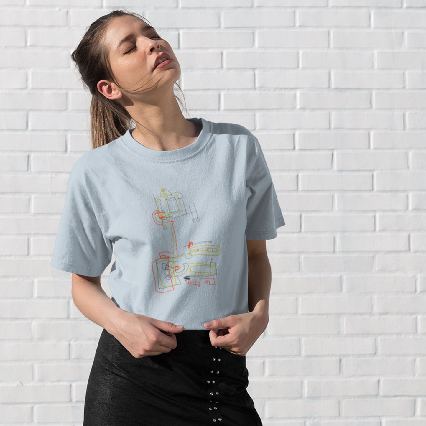 Woman wearing a light blue t-shirt with a colorful abstract drawing on a white brick background.