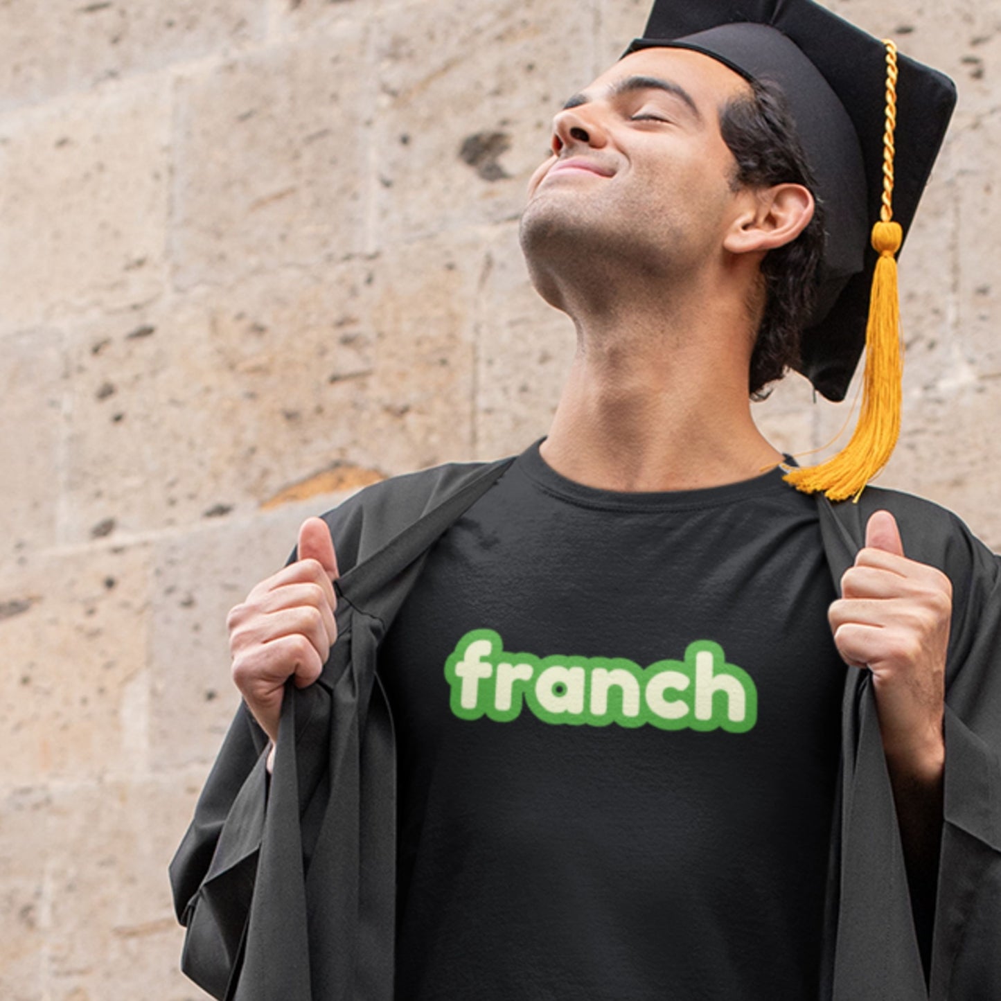 Proud graduate wearing a black t-shirt with humorous colorful franch text outside.