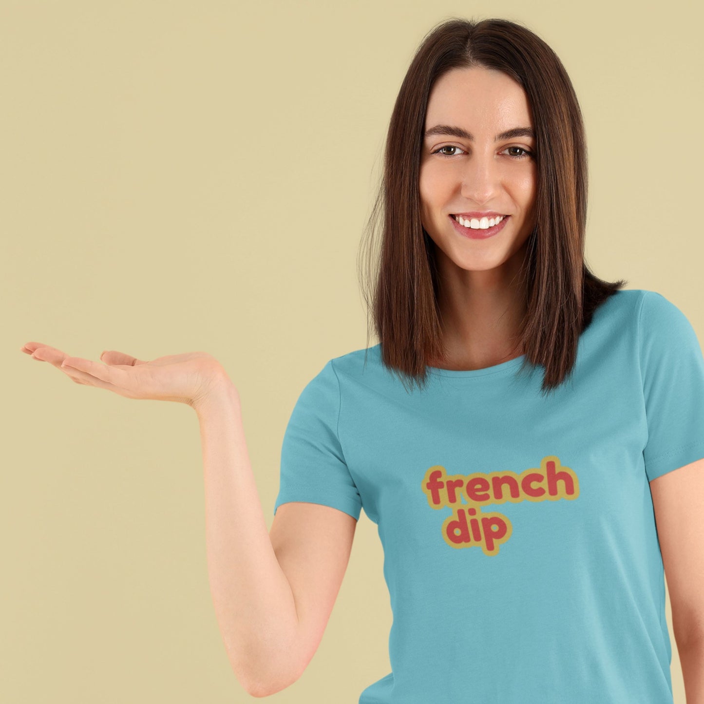 Smiling woman wearing a turquoise t-shirt with multicolored 'french dip' text on a beige background is waiting for a french dip to be placed in her hand.