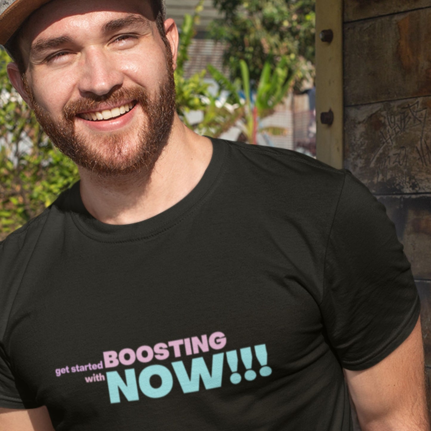 Smiling man wearing a black t-shirt with humorous colorful text outdoors.