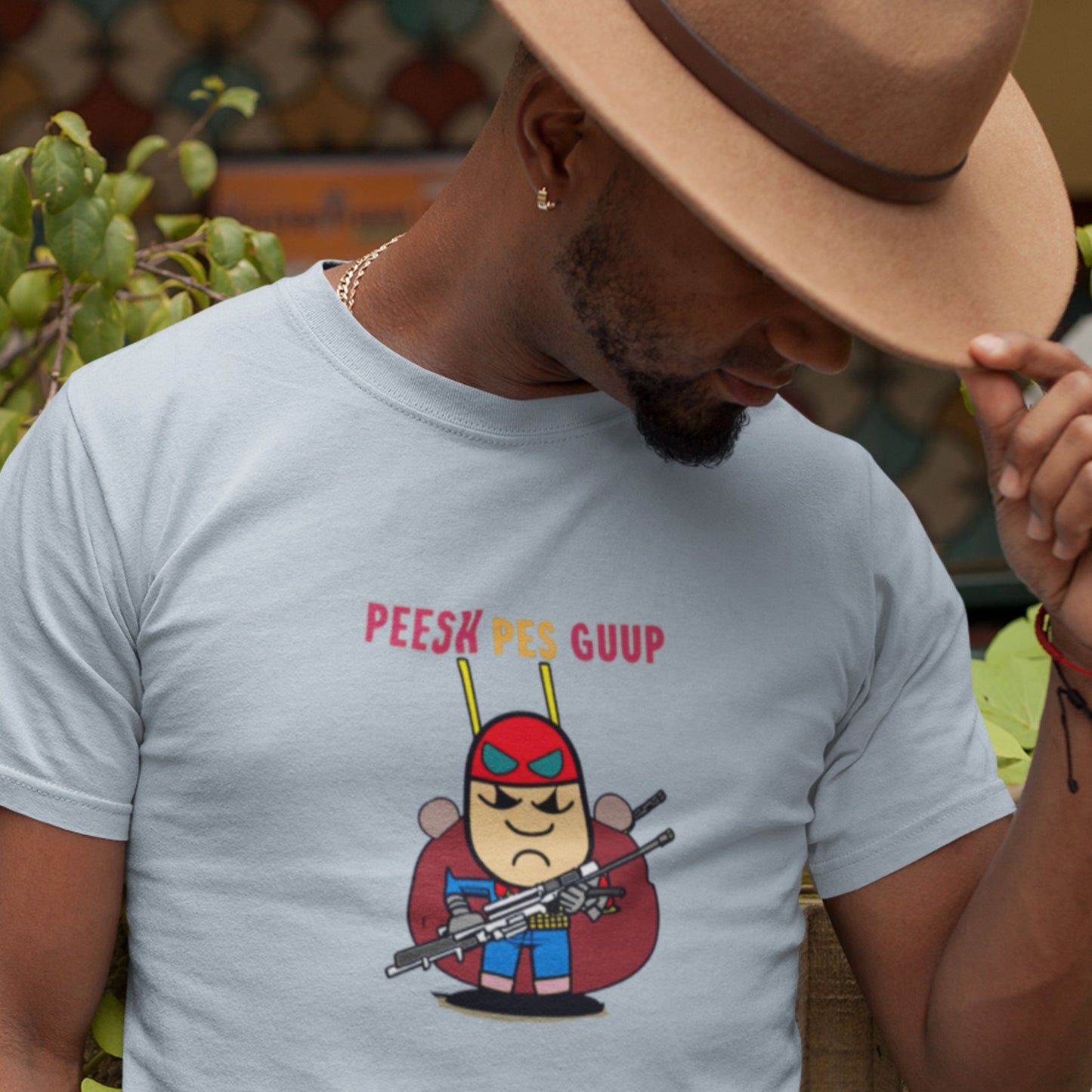 Cowboy man wearing a light blue t-shirt with a fun, colorful cartoon character illustration outside wearing a hat.