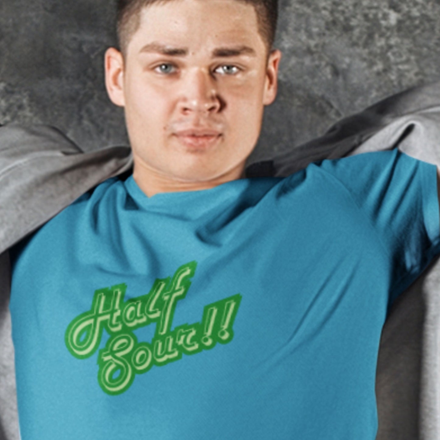 Person wearing a blue shirt with 'Half Sour!!' text, sitting against a gray background