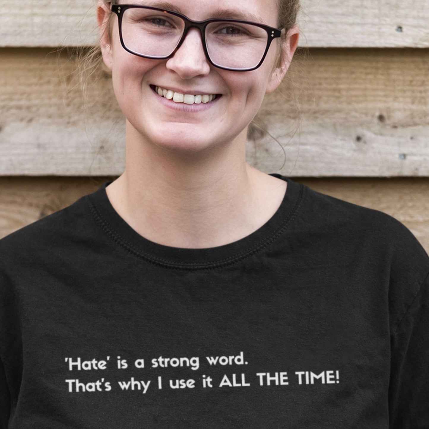 Person wearing a black t-shirt with a humorous quote, standing against a wooden background.