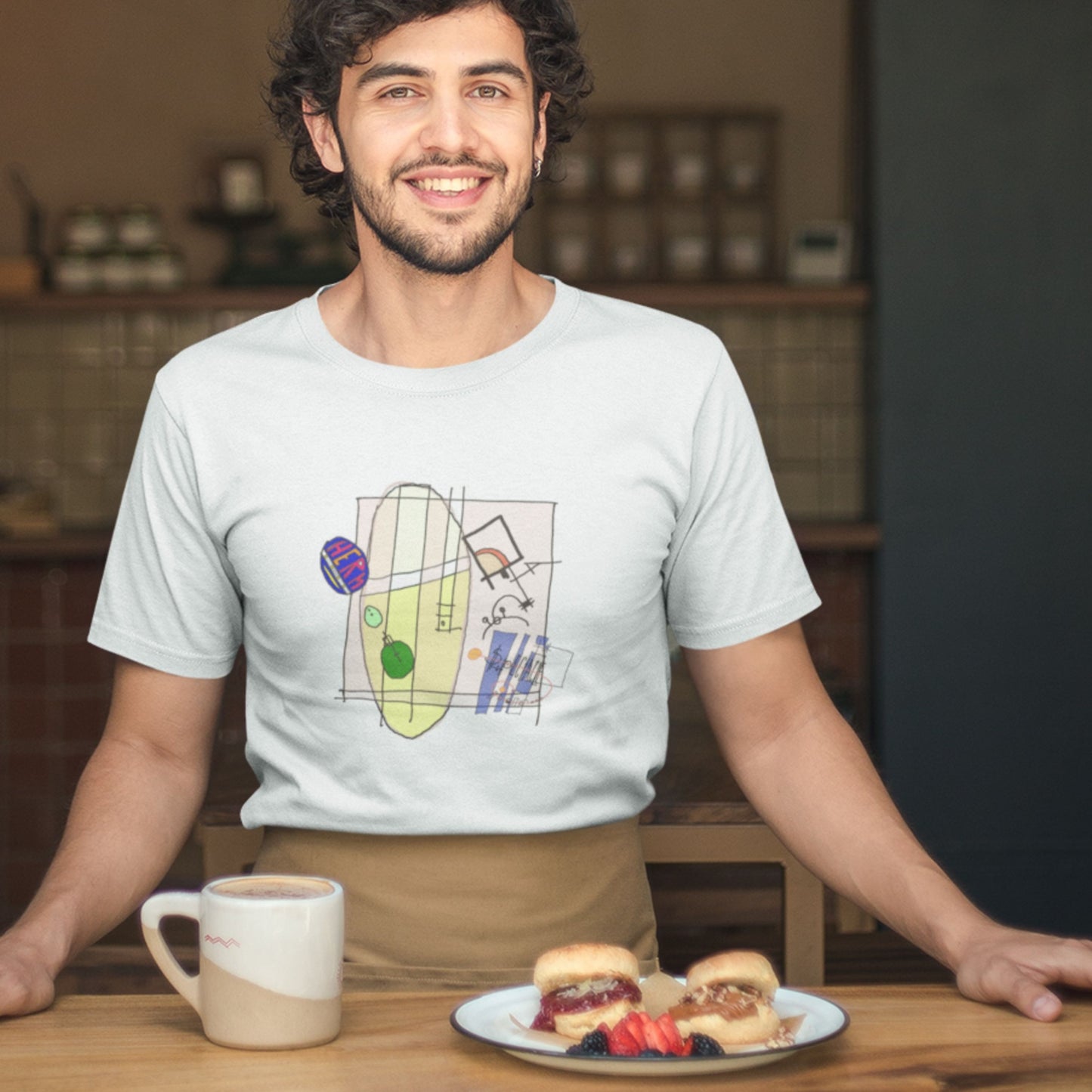 This guy wearing a white t-shirt with a colorful abstract system drawing in a kitchen.