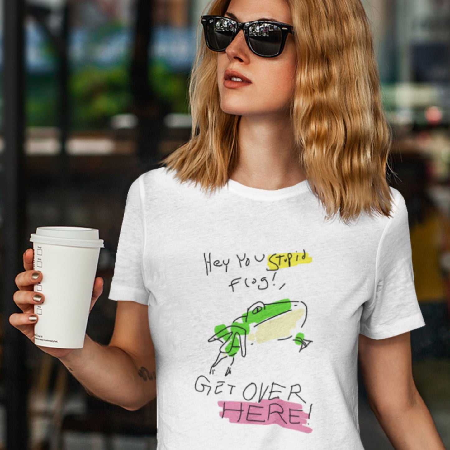 Person wearing a white t-shirt with a graphic design and holding a coffee cup.