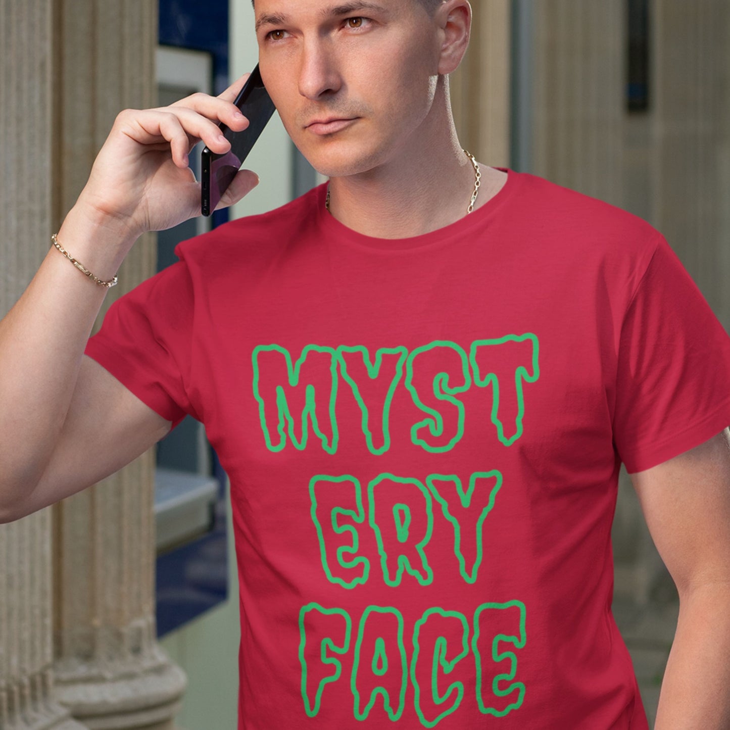 Man wearing a red t-shirt with 'MYSTERY FACE' in green text, talking on a phone.