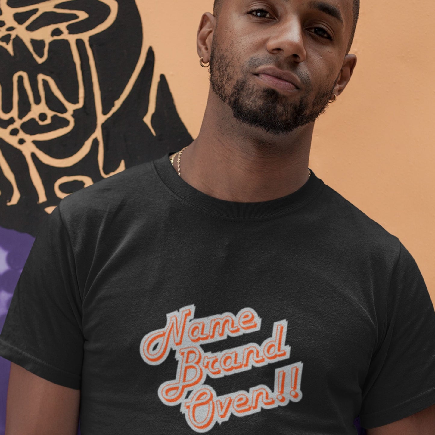 Man wearing a black t-shirt with 'Name Brand Over!' text against a colorful background.