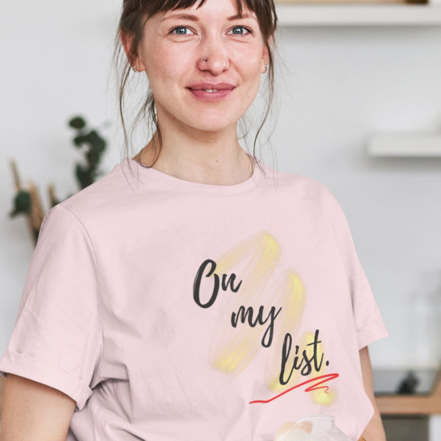 Woman wearing a pink t-shirt with 'on my list.' text and graphics in a casual setting