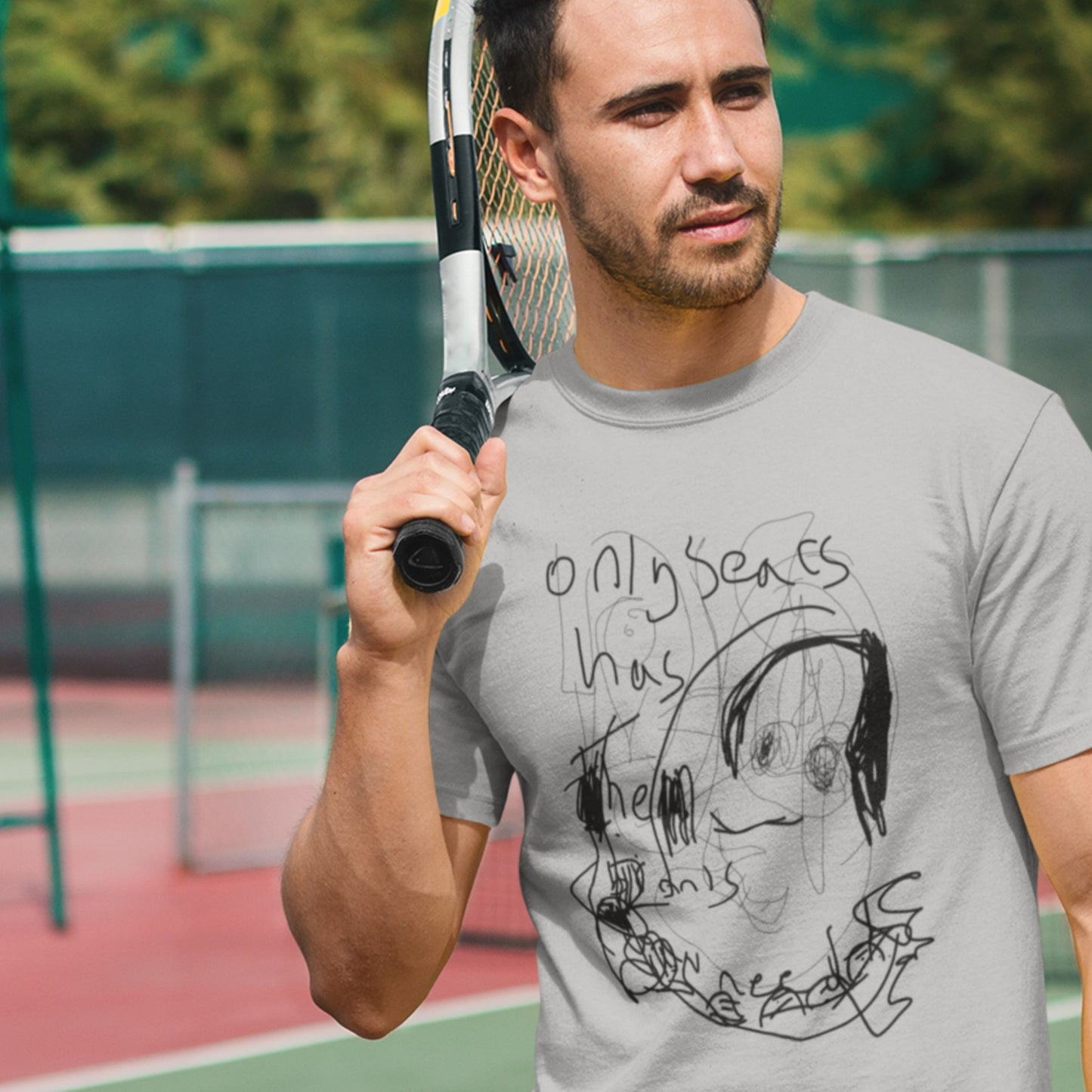 Man holding a tennis racket on a tennis court wearing a gray t-shirt with a graphic design.