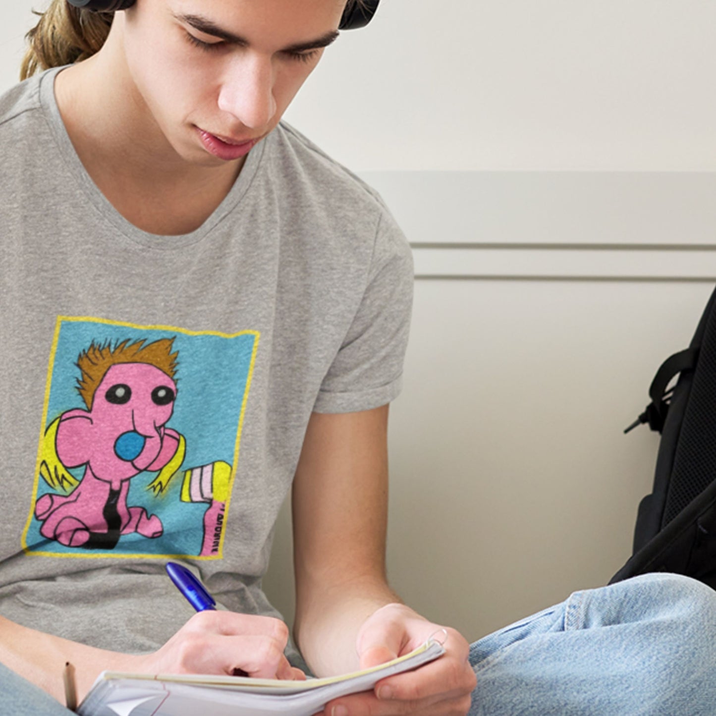 Man wearing a grey t-shirt with a fun, colorful cartoon illustration in his bedroom.