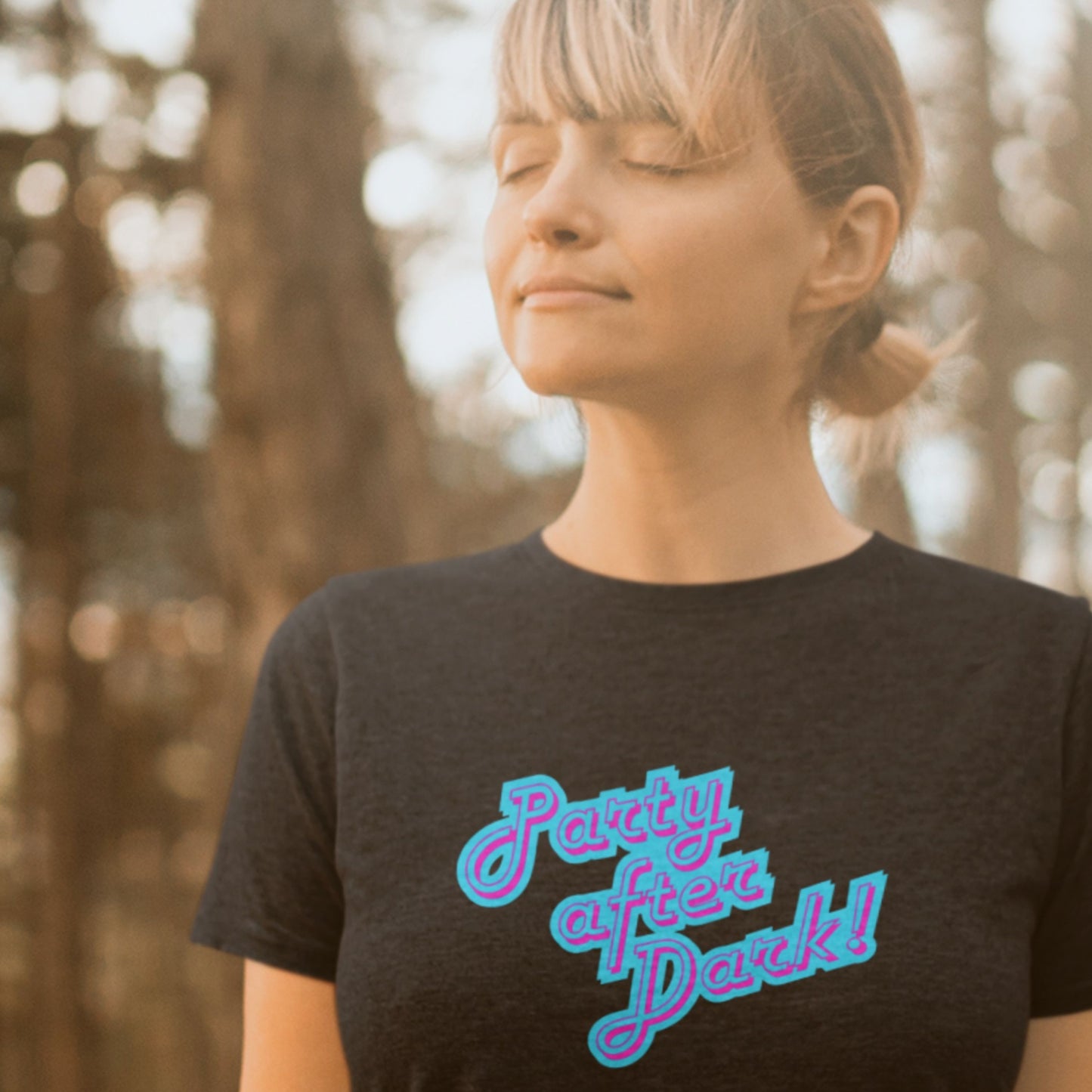 Woman relaxing wearing a black t-shirt with humorous colorful text outdoors.