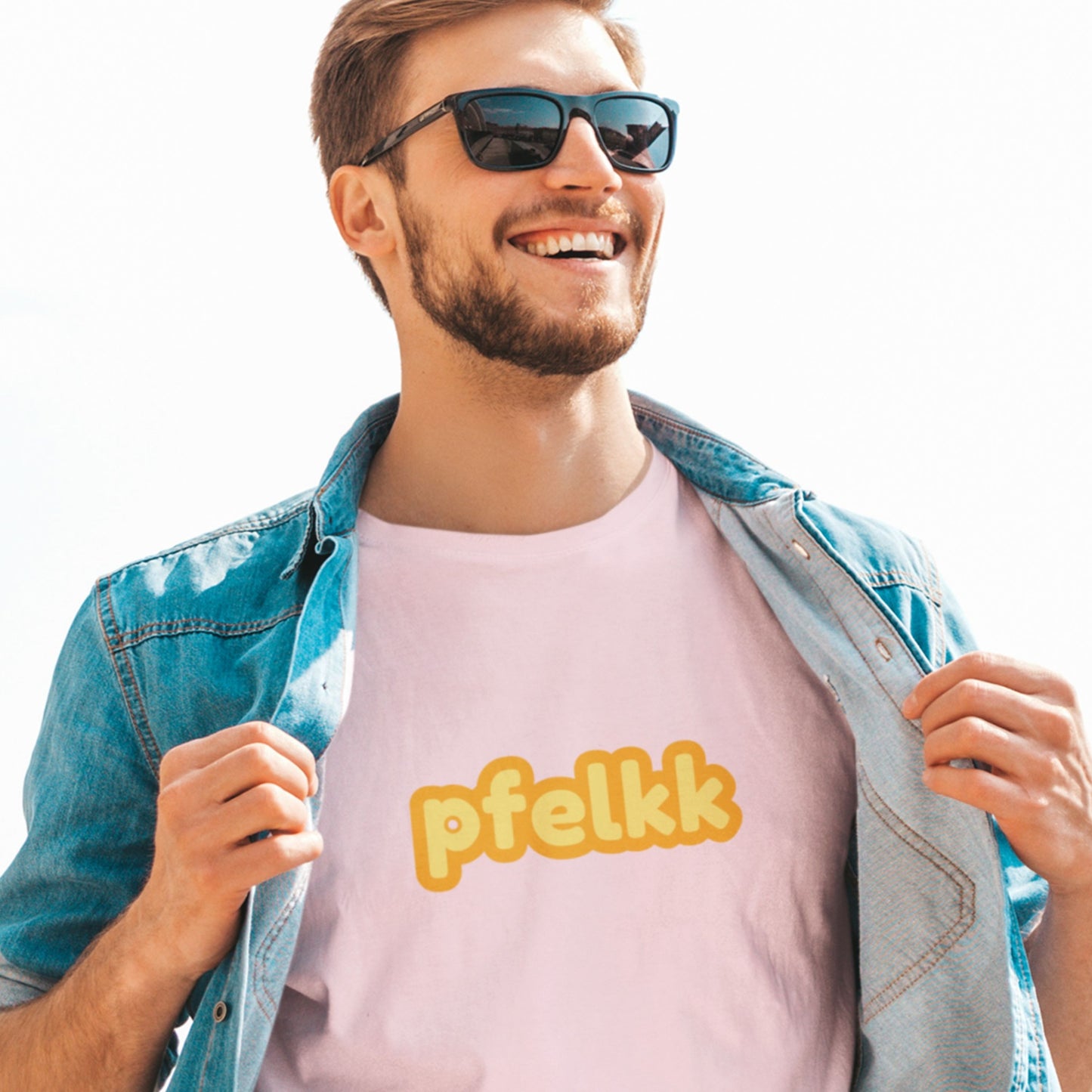 Happy man wearing a pink tee with multicolored 'pfelkk' text on a clear day outside.