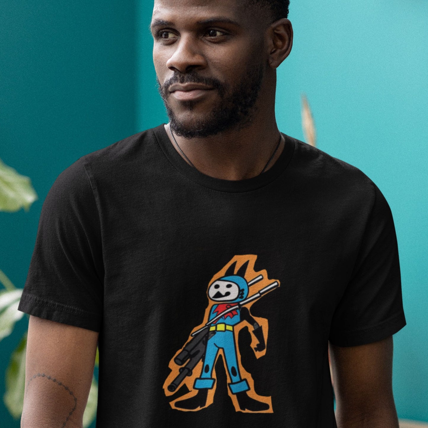 Man wearing a black t-shirt with a fun, colorful cartoon hero illustration in a blue room.