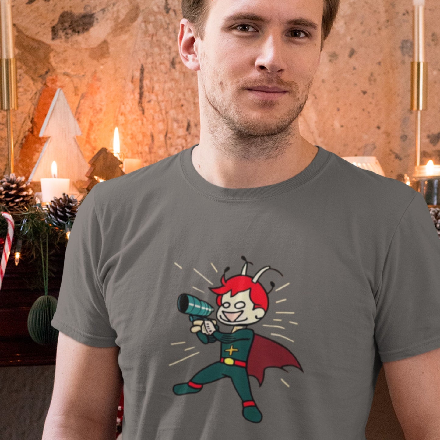 Holiday man wearing a dark grey t-shirt with a colorful cartoon illustration in front of a hearth.