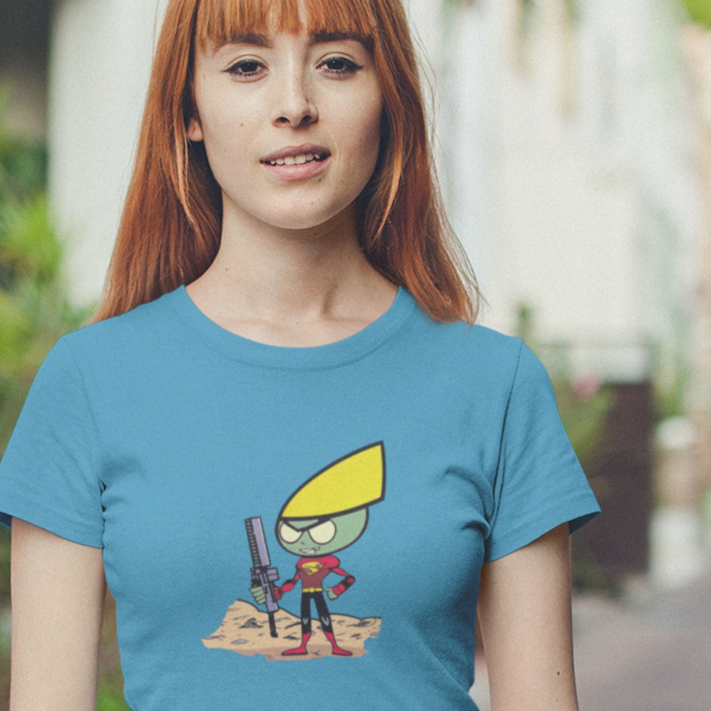 Smiling woman wearing an aqua blue shirt with a fun, colorful cartoon illustration outdoors.