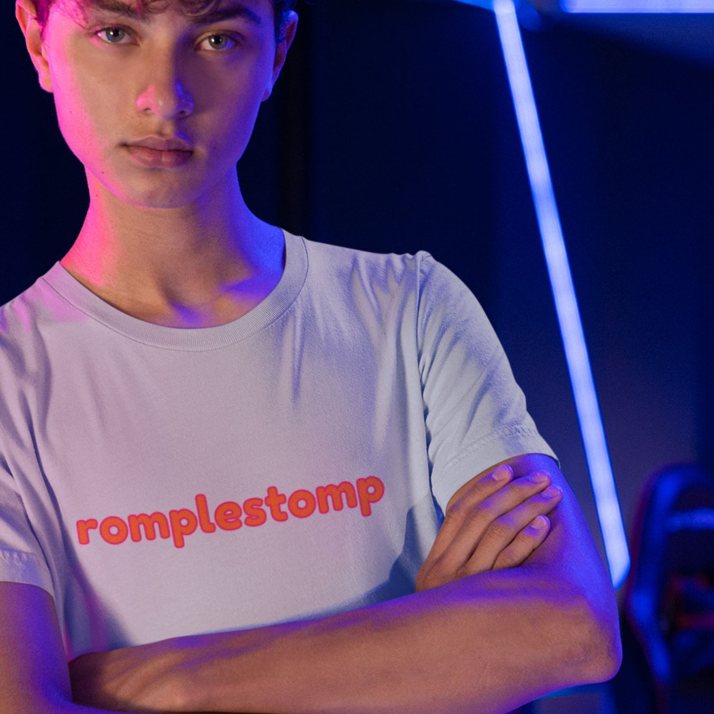 Sullen teen wearing a light grey t-shirt with multicolored 'romplestomp' text in a laser place.