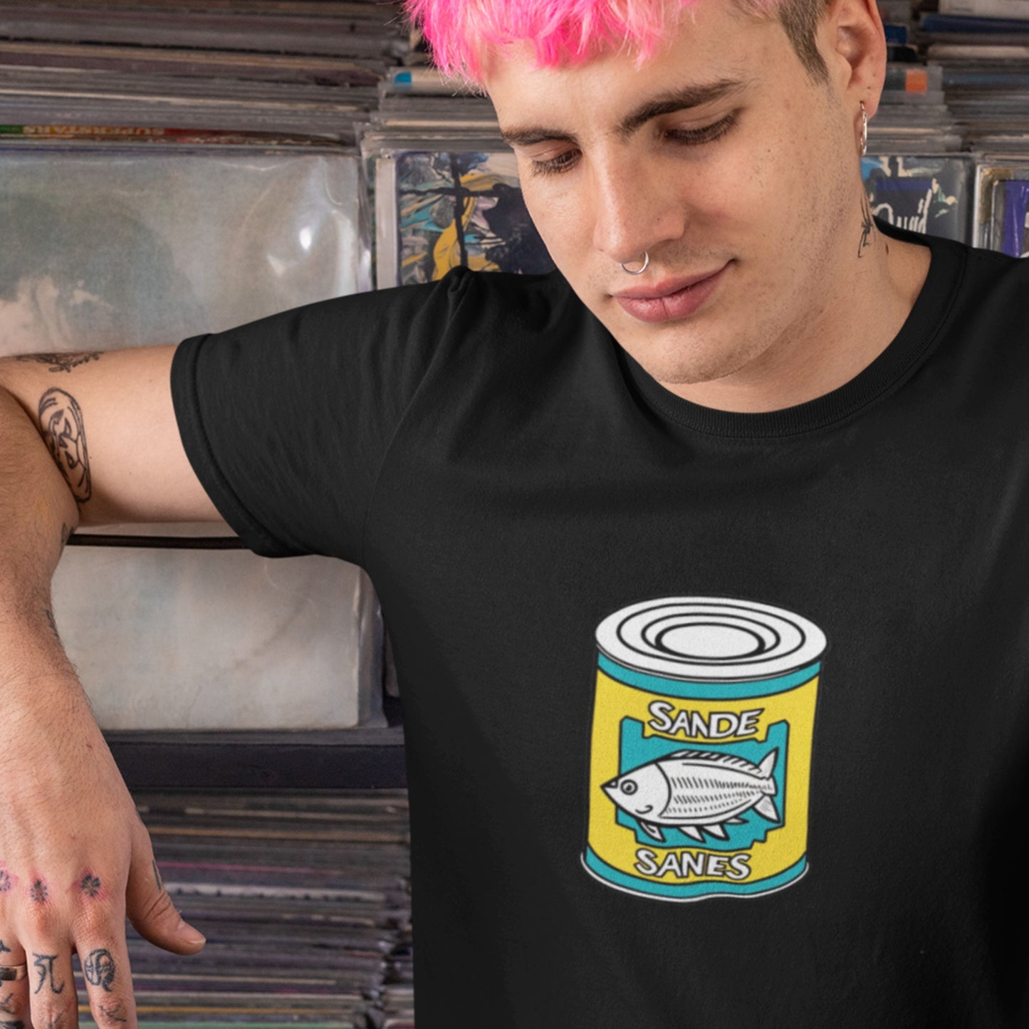 Person wearing a black t-shirt with a can design in front of a record collection