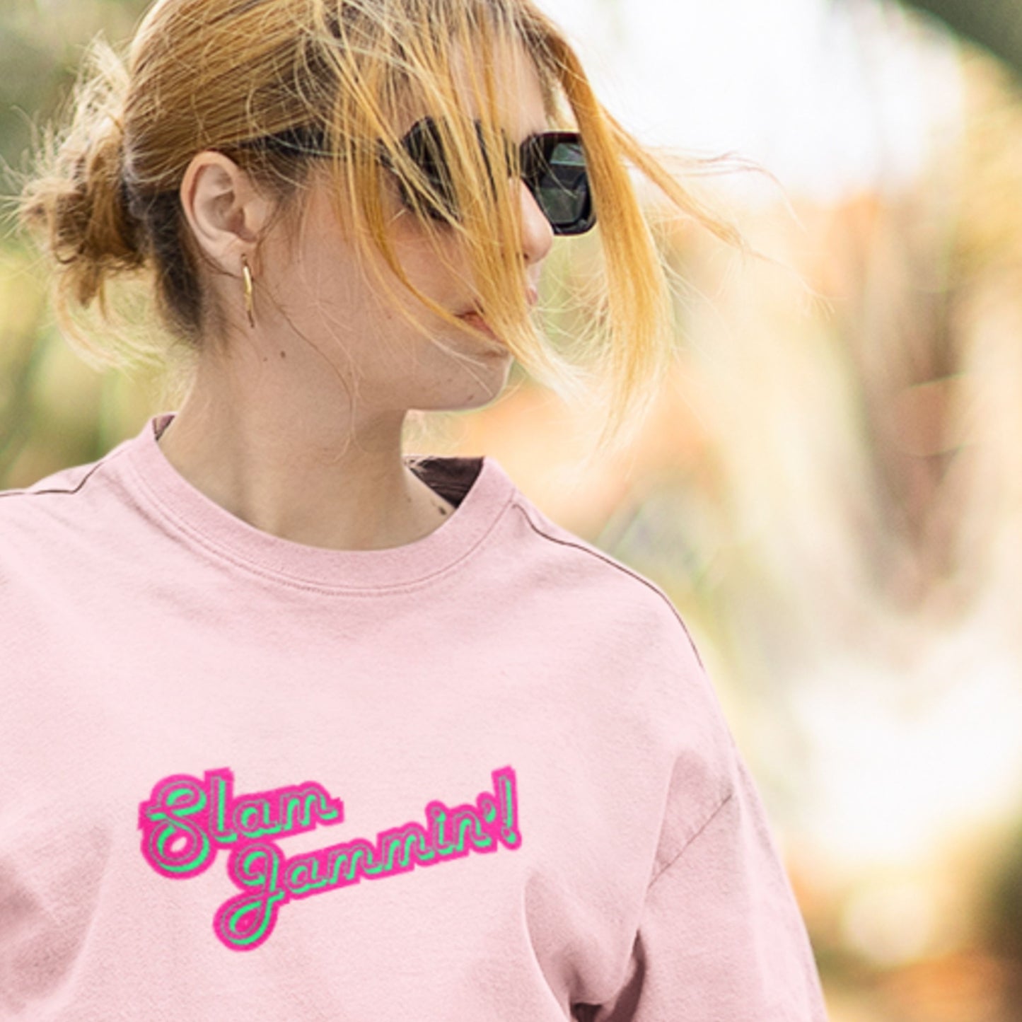 Woman wearing a pink tee with multi-colored humorous text outdoors.