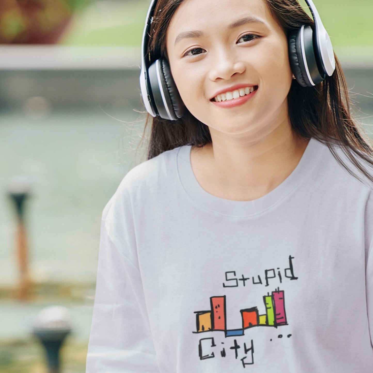 Person wearing headphones and a shirt with 'Stupid City' design outdoors.