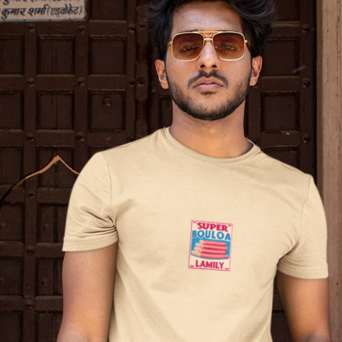 Man in sunglasses wearing a cream colored shirt with a brand logo for a bologna brand against a doorway.
