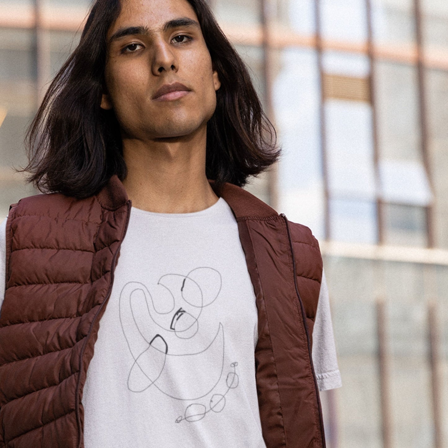 Person wearing a white t-shirt with a design and a brown puffer jacket indoors.