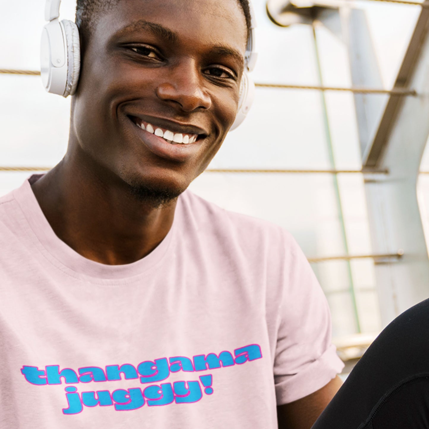 Man wearing headphones and a pink t-shirt with colorful text, sitting indoors.