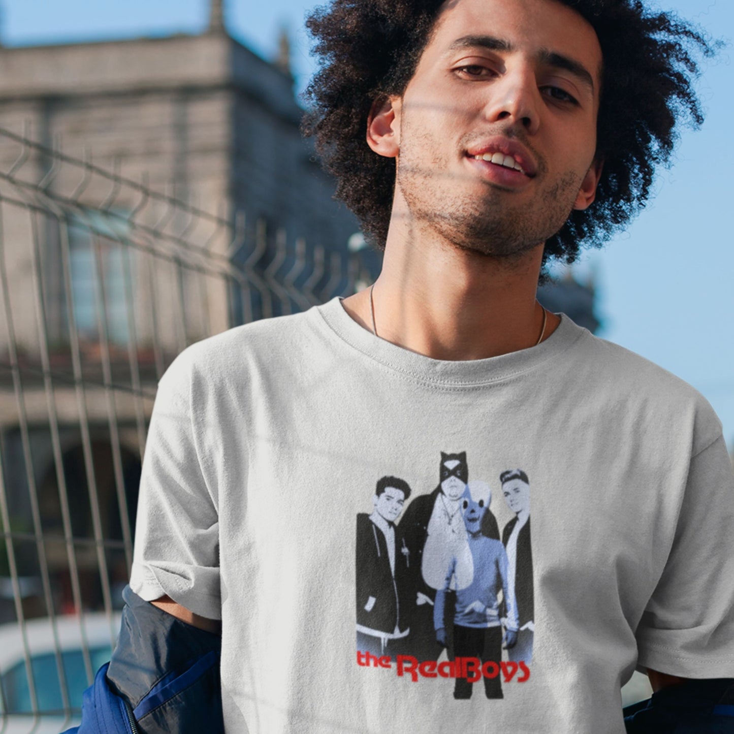 Man wearing a t-shirt with a graphic design of four people and 'the RealBoys' text, standing outdoors.
