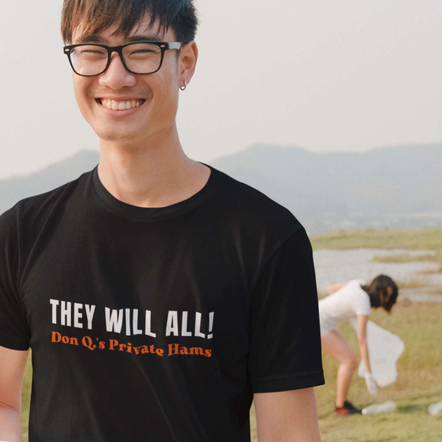 Person wearing a black t-shirt with text, standing outdoors with mountains in the background.